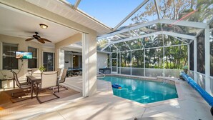 Una piscina interior con cerramiento de vidrio, un ventilador de techo y un área de estar con televisión.