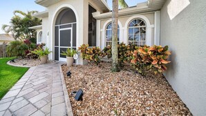 Una casa moderna con un camino de piedra que conduce a la entrada, rodeada de un jardín cuidado con diversas plantas y una palmera.