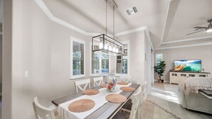 Un comedor con una mesa de madera, sillas blancas y una lámpara colgante.