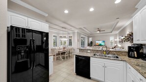 Una cocina moderna con armarios blancos, un refrigerador negro y una zona de comedor con mesa y sillas.