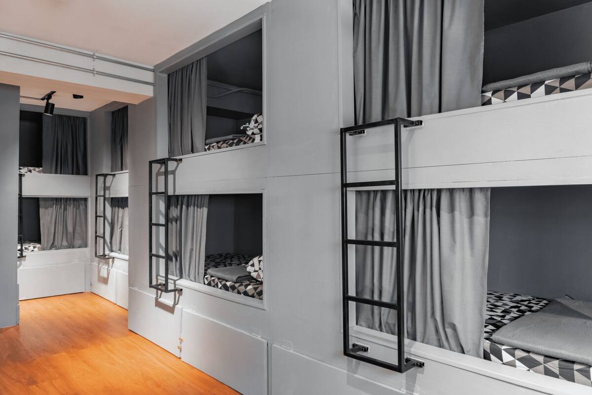 A room with bunk beds, a wooden floor, and a window with curtains.