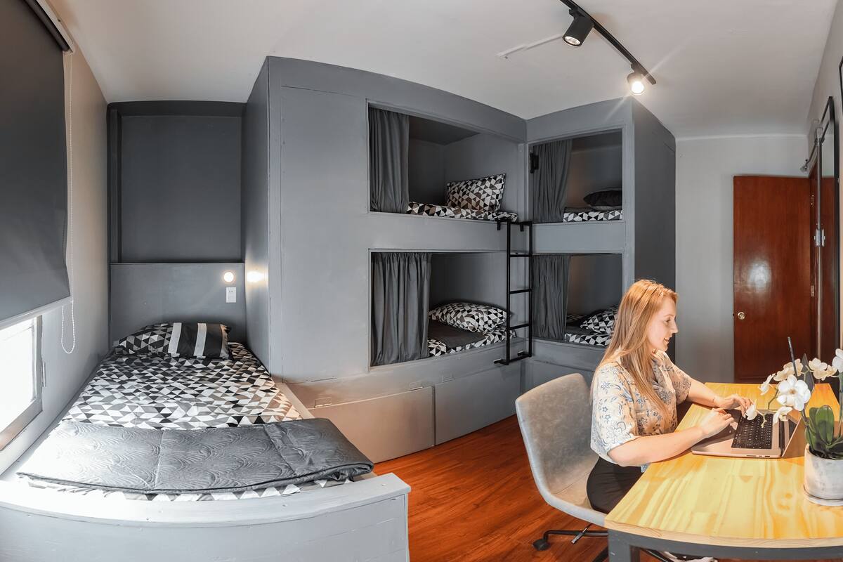 A compact room with a curved bed, a desk, and a laptop. There are bunk beds in the background.