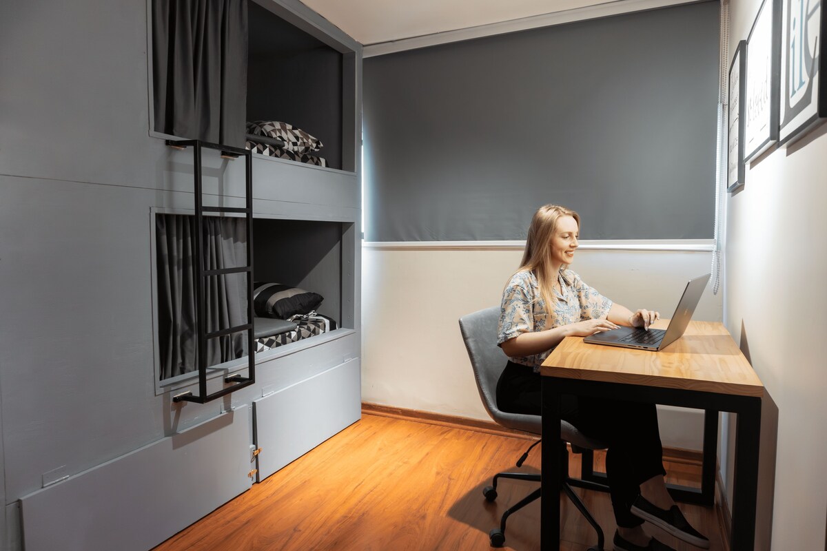 A room with a bed, a desk with a laptop, a chair, and a window with curtains.