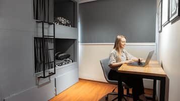A room with a bed, a desk with a laptop, a chair, and a window with curtains.
