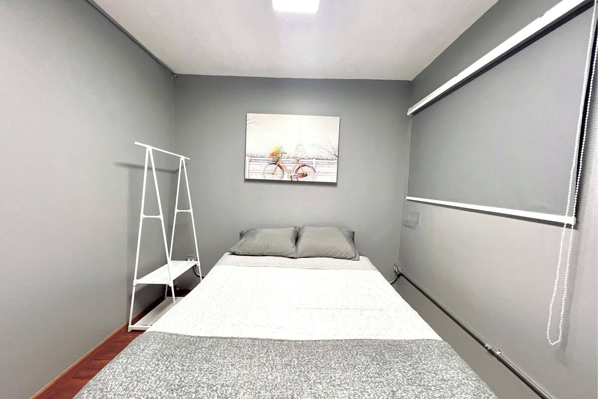 A small, modern bedroom with a bed, a ladder, a painting, and a window.