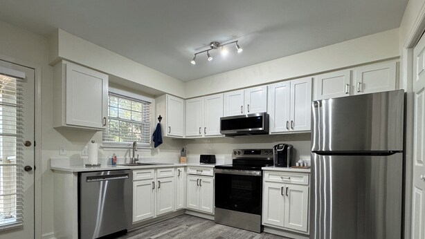 A modern kitchen with white cabinets, stainless steel appliances, and a herringbone wood floor. - Down to the Wire, Cozy 2-bedroom condo with WiFi and AC in welcoming Auburn (Auburn)
