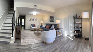 A living room with a staircase, a grey sofa, a coffee table, and a floor lamp. - Down to the Wire, Cozy 2-bedroom condo with WiFi and AC in welcoming Auburn (Auburn)