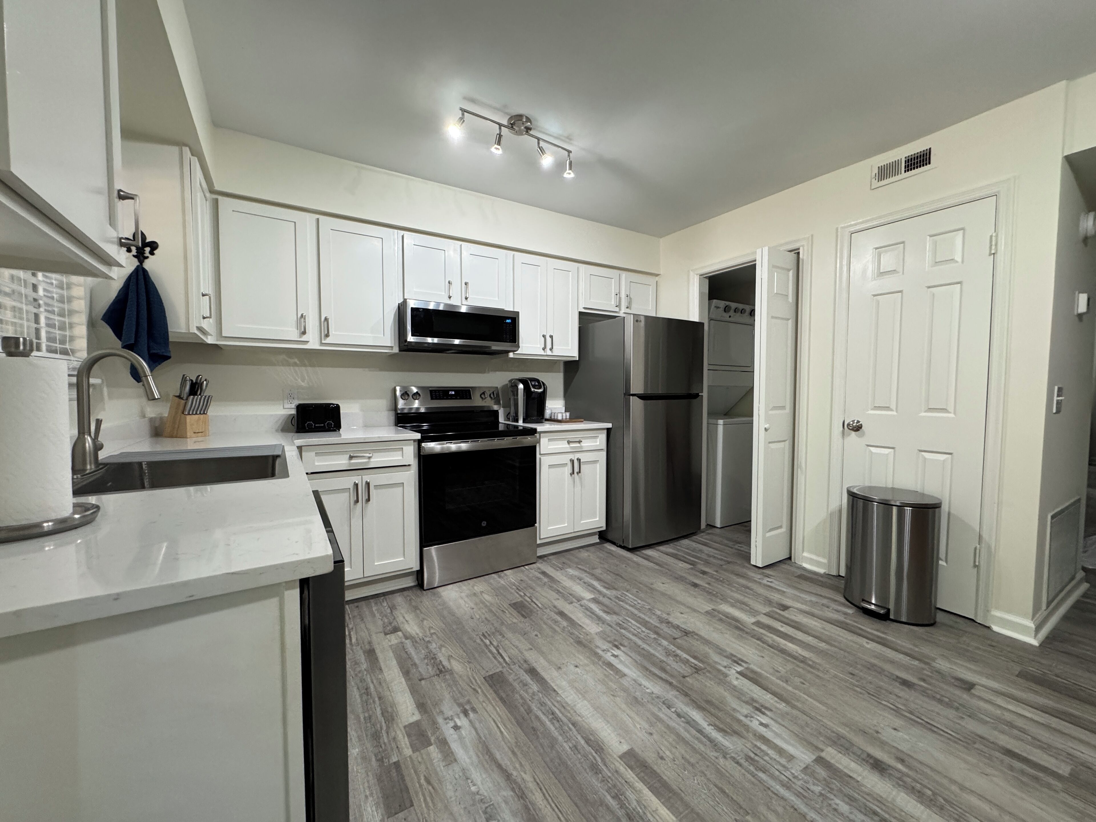 A modern kitchen with white cabinets, stainless steel appliances, and a wooden floor.