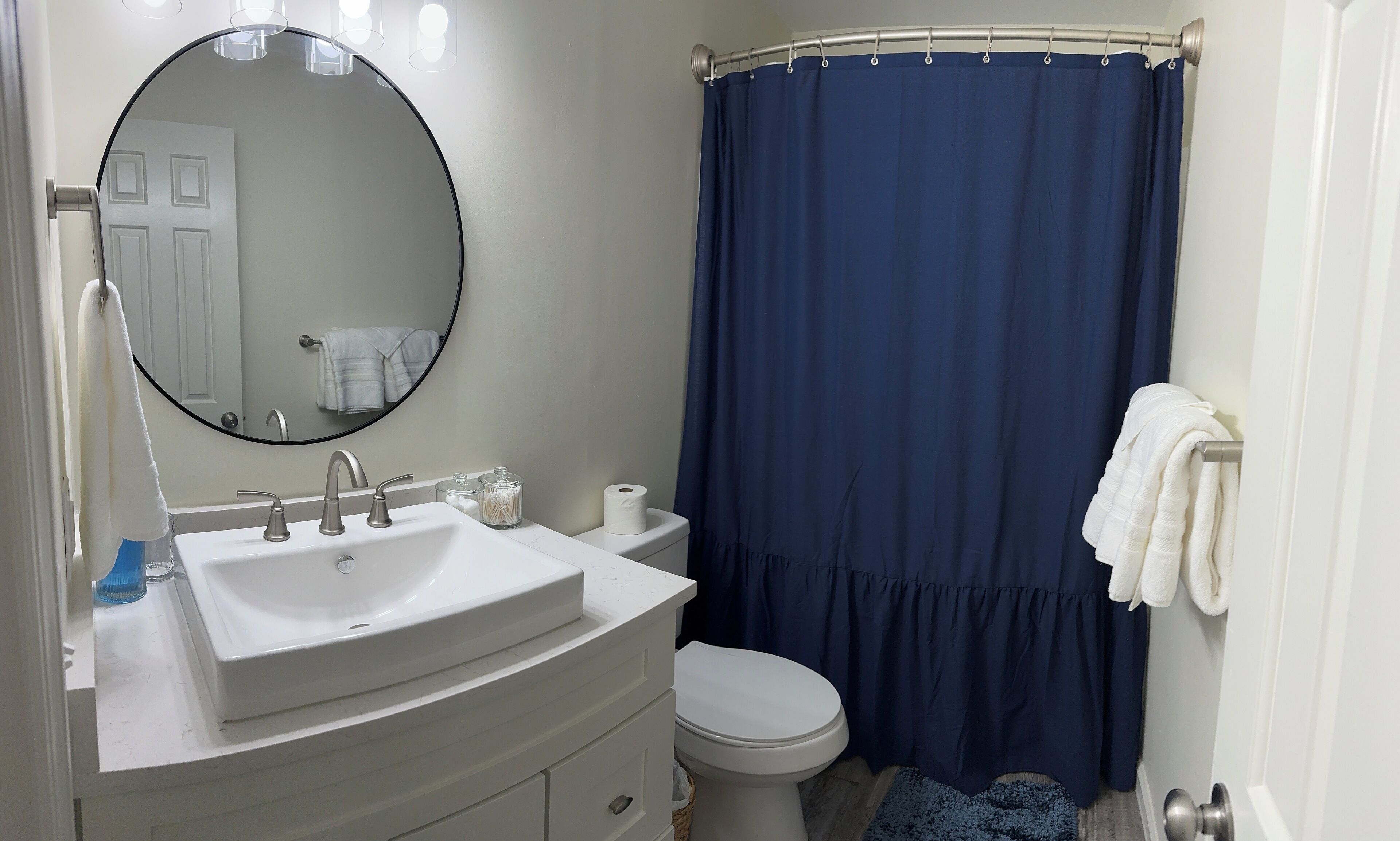 A bathroom with a white sink, a toilet, a blue shower curtain, and a mirror.