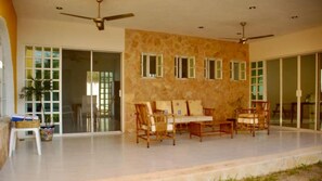 Relax in a spacious room with a high ceiling, featuring a comfortable sofa set and a sliding glass door leading to an outdoor area.
