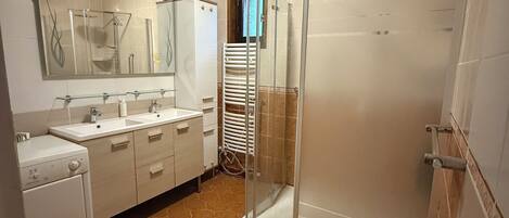 A modern bathroom with a glass-enclosed shower, a large mirror, and a built-in washing machine.