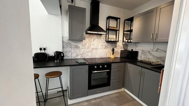 Une cuisine moderne avec des meubles gris, une cuisinière noire et deux tabourets de bar.
