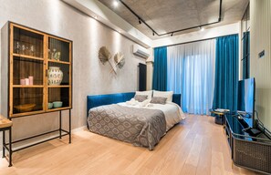 Un dormitorio moderno con una cama grande, un aparador de madera con puertas de cristal y un ventanal con cortinas azules.
