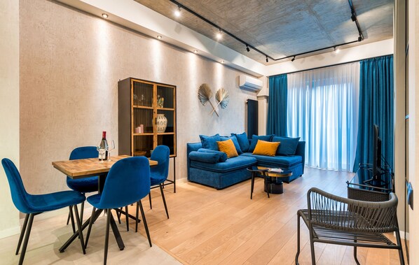 Una sala de estar moderna con una mesa de comedor de madera, sillas azules, un sofá azul con cojines amarillos y una silla de mimbre.