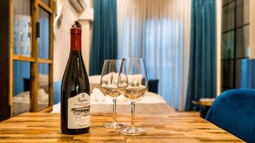 A bottle of wine and two glasses on a wooden table in a room with a bed and curtains in the background.