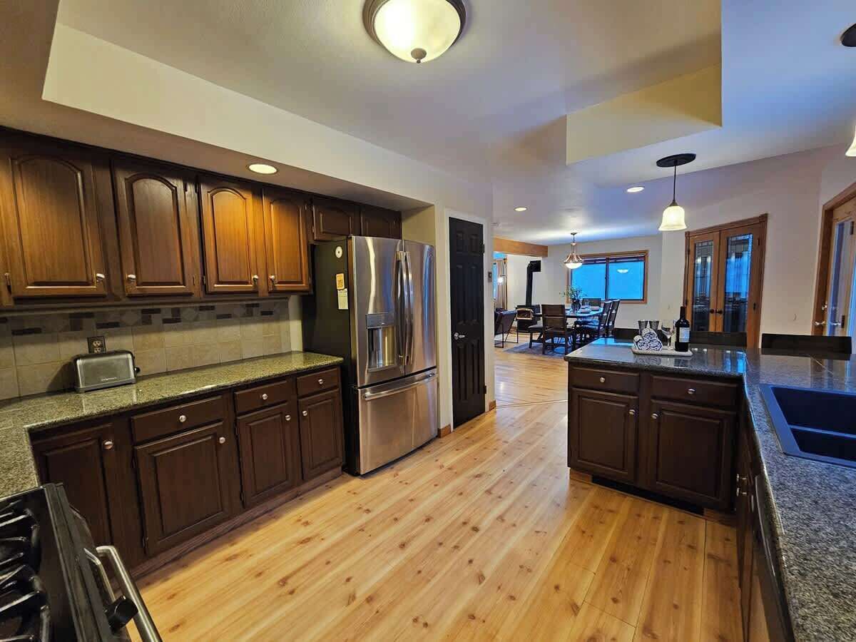 A modern kitchen with dark wooden cabinets, stainless steel appliances, and a wooden floor.