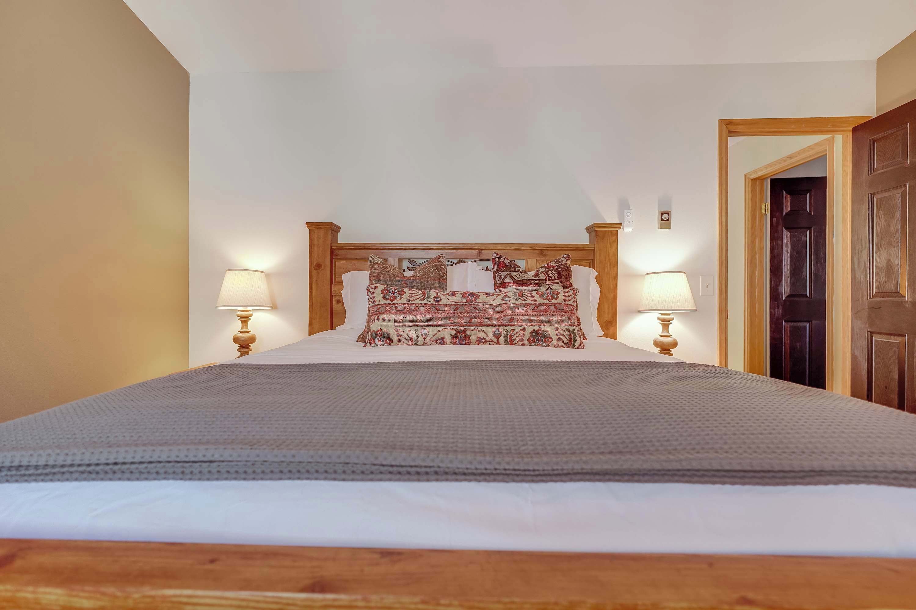 A neatly made bed with a wooden headboard, two bedside lamps, and a patterned pillow.