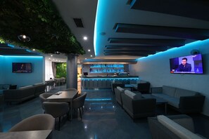A modern lounge area with a bar, seating, and a TV screen. - Hotel Gjuta (Farkë)