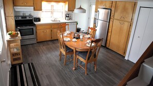 Una cocina con armarios de madera, una mesa de comedor para cuatro personas y un refrigerador.