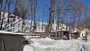 Un paisaje nevado con una cabaña, un área cercada y suelo cubierto de nieve.