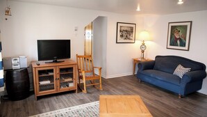 Una sala de estar con televisión, muebles de madera, un sofá azul y cuadros en la pared.