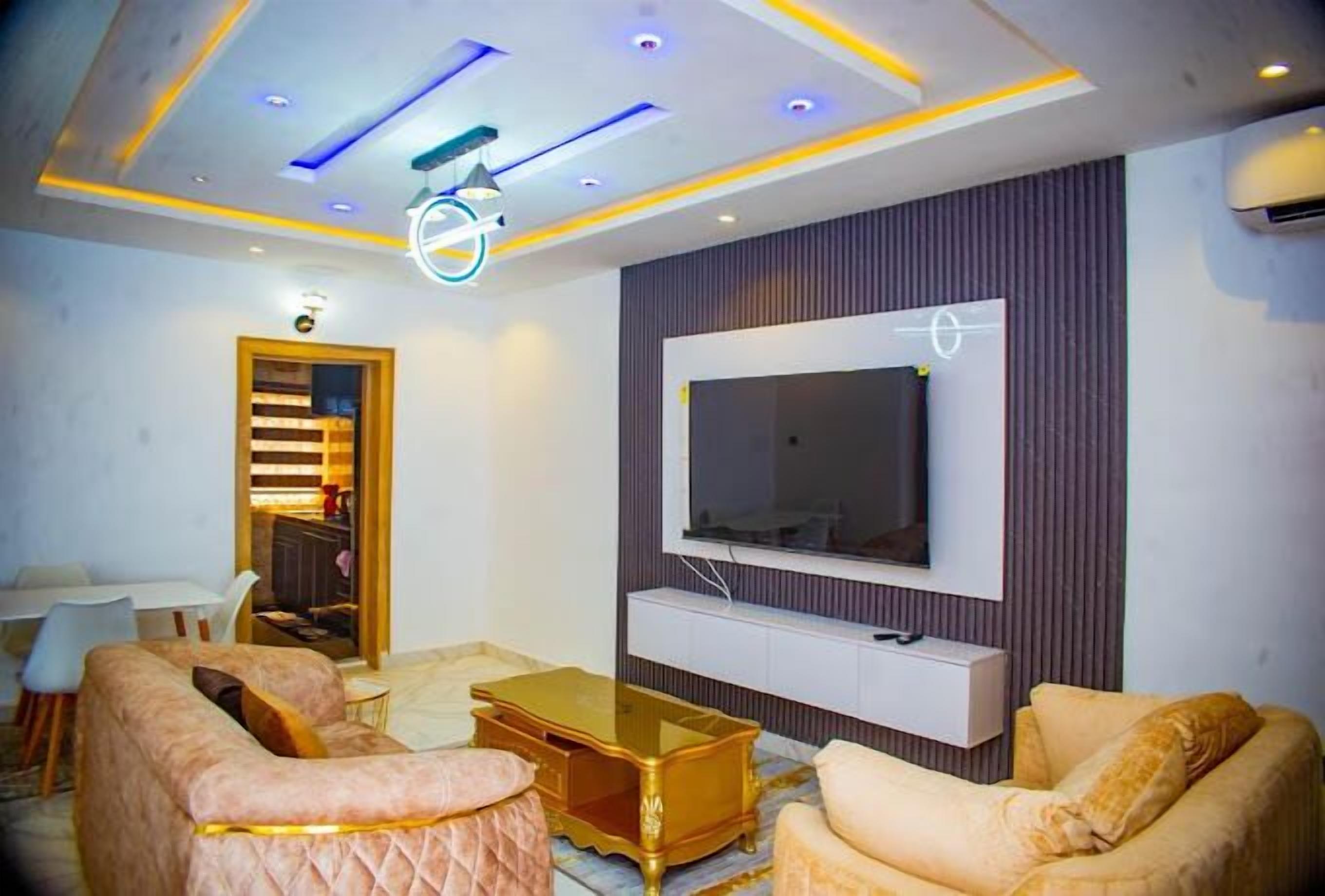 A modern living room with a flat-screen TV mounted on a wall, a glass coffee table, and two sofas.