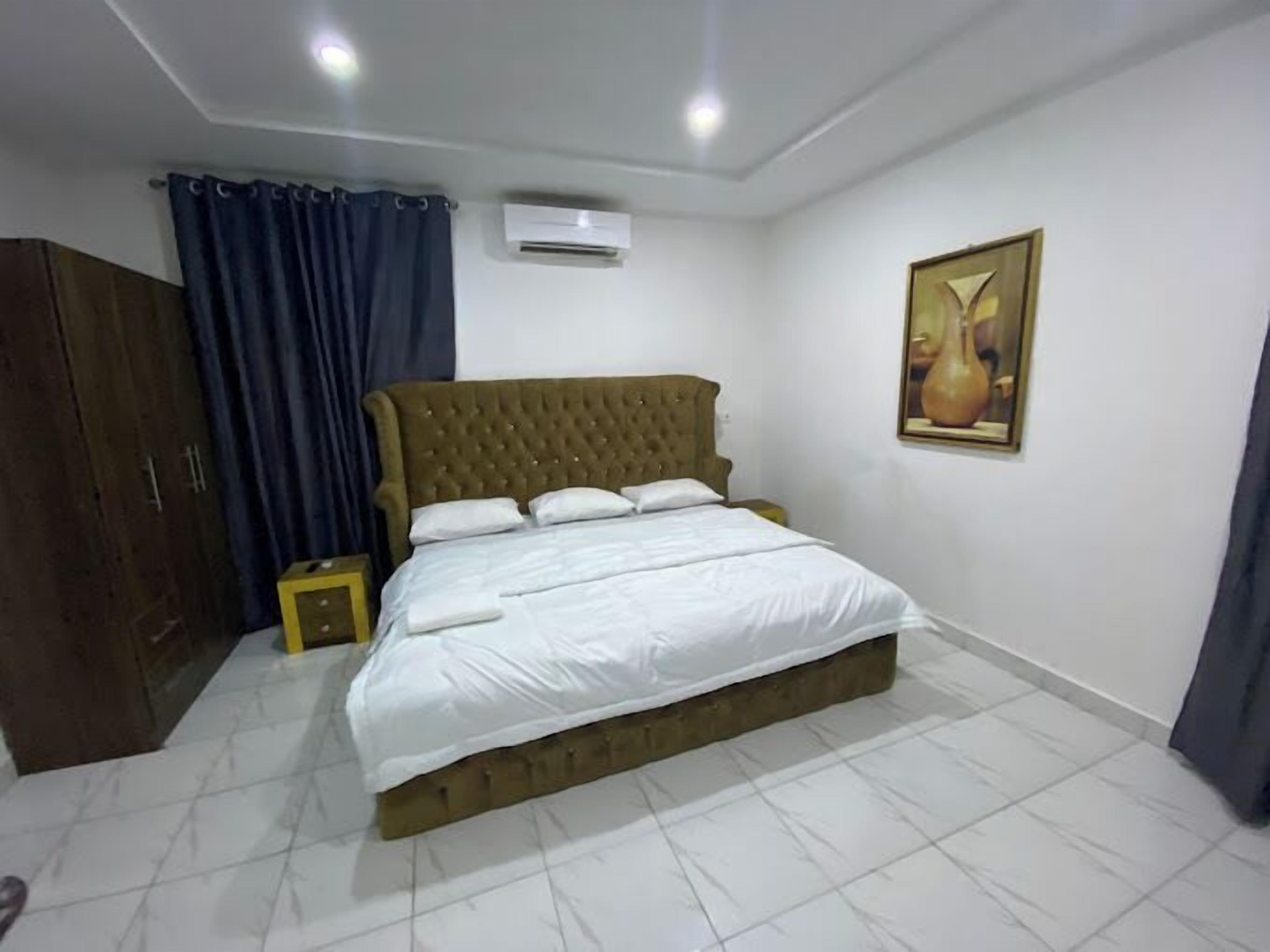 A bedroom with a large bed, a wardrobe, an air conditioning unit, and a painting on the wall.