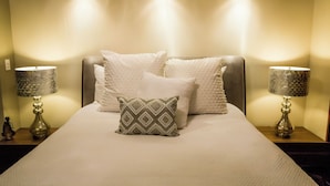 A neatly made bed with white linens and decorative pillows, flanked by two lamps on wooden nightstands.