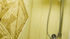 A bathroom with a shower, tiled walls, and a mosaic tile design on the left wall.