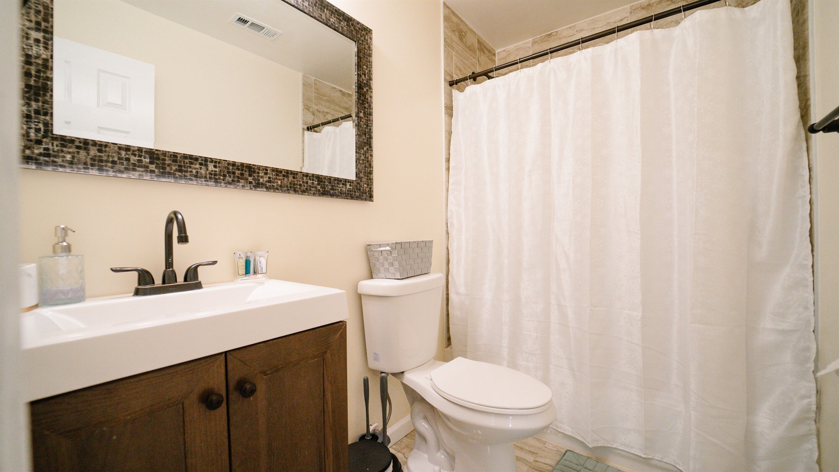 Une salle de bain avec un lavabo blanc, un miroir, des toilettes et un rideau de douche.