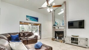 A spacious living room with a leather sofa, a fireplace, a television, and a large window.
