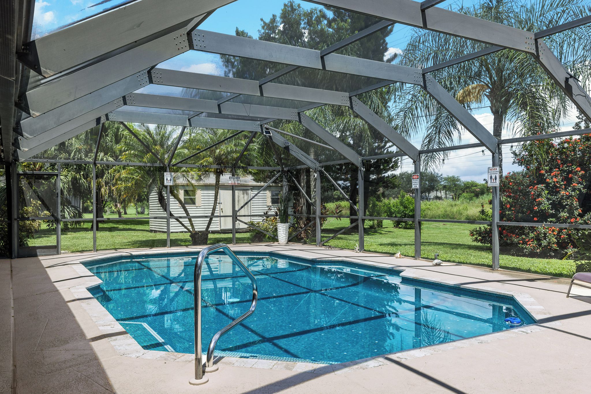 Une piscine couverte avec une structure en métal, entourée de verdure et sous un ciel dégagé.
