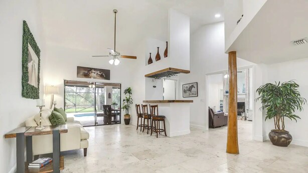 A spacious living area with a ceiling fan, a dining table with chairs, a sofa, and a large potted plant.