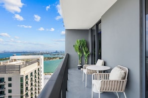 A balcony with a view of the ocean and cityscape, featuring a table and chairs.