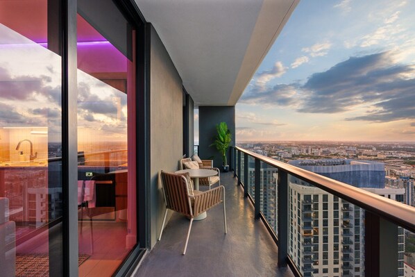 A balcony with a view of the city, a round table with chairs, and a potted plant.