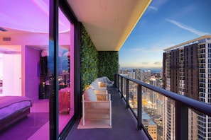 A balcony with a city view, a bed, a seating area, and a green wall.