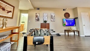 A spacious living room with a foosball table, a television displaying a news channel, and a staircase leading to an upper level. - Relax @ Retreat Pool Hot Tub Billiards Game SF Bay (Santa Clara)
