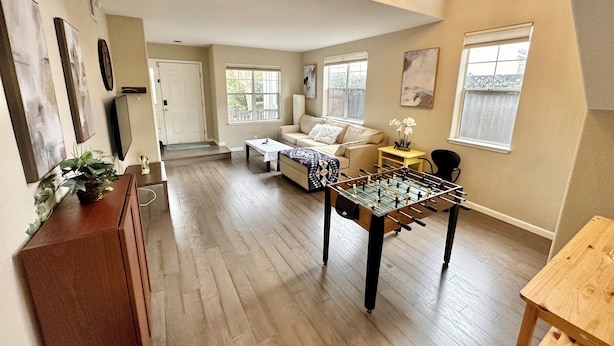A spacious living room with a foosball table, a sofa, and a coffee table. There are large windows providing natural light and a view of the outside. - Relax @ Retreat Pool Hot Tub Billiards Game SF Bay (Santa Clara)