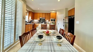 A dining area with a table set for four, flanked by wooden chairs, a kitchen in the background, and a window with blinds. - Relax @ Retreat Pool Hot Tub Billiards Game SF Bay (Santa Clara)