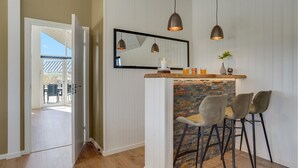 A modern kitchen with a stone fireplace, two pendant lights, a mirror, and a bar area with stools.