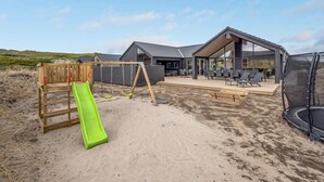 A modern outdoor area with a wooden play structure, a green slide, and a seating area with tables and chairs.