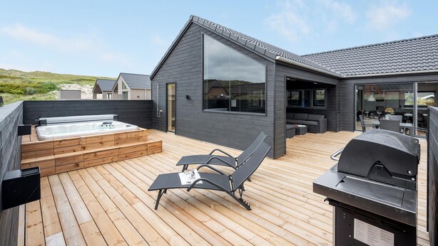 A modern outdoor deck with a hot tub, lounge chairs, and a grill area.
