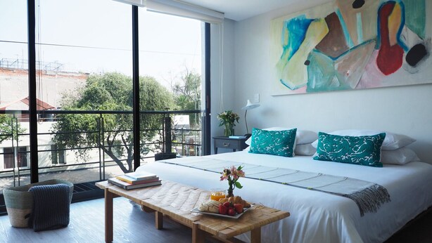 Ein modernes Schlafzimmer mit einem großen Bett, einer hölzernen Bank und Blick ins Freie durch große Fenster.