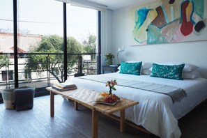 Ein modernes Schlafzimmer mit einem großen Bett, einer hölzernen Bank und Blick ins Freie durch große Fenster.