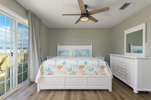 Ein Schlafzimmer mit einem Bett, einem Schminktisch, einem Deckenventilator und einem großen Fenster.