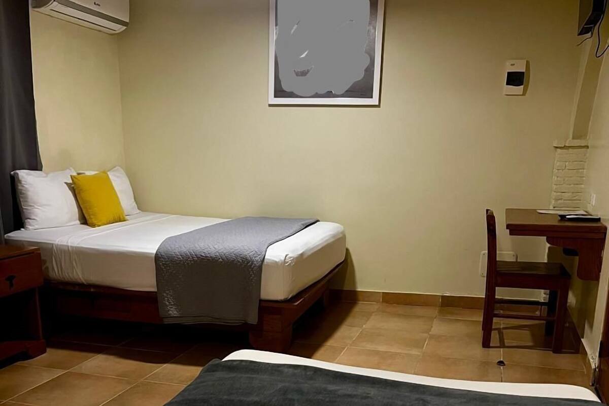 A hotel room with a bed, a desk, and an air conditioning unit.