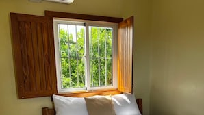 A bedroom with a bed, wooden headboard, a window with a view of greenery, and a wall-mounted air conditioner. - Hotel Yamilí (Punta Cana)