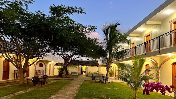 A courtyard with a pathway, seating areas, and a building with arched windows and balconies. - Hotel Yamilí (Punta Cana)