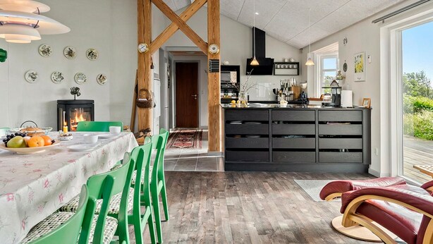 Una cocina moderna con un arco de madera central, una zona de comedor con sillas verdes y vistas al exterior.