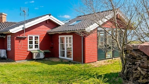 Una casa roja con techo de tejas, chimenea y un pequeño garaje adosado.